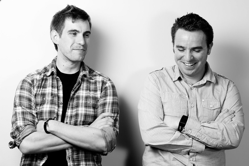 Two colleagues caught mid-conversation in a studio. One laughing, one watching, both unposed.