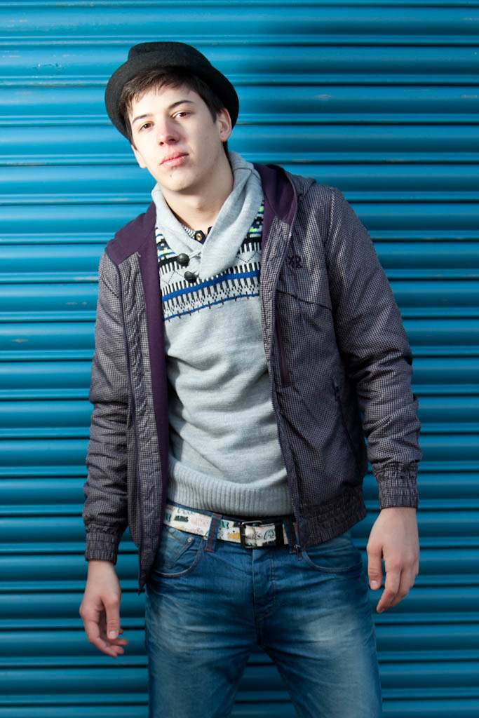 Street portrait against a blue-painted shutter. Unposed, available light.